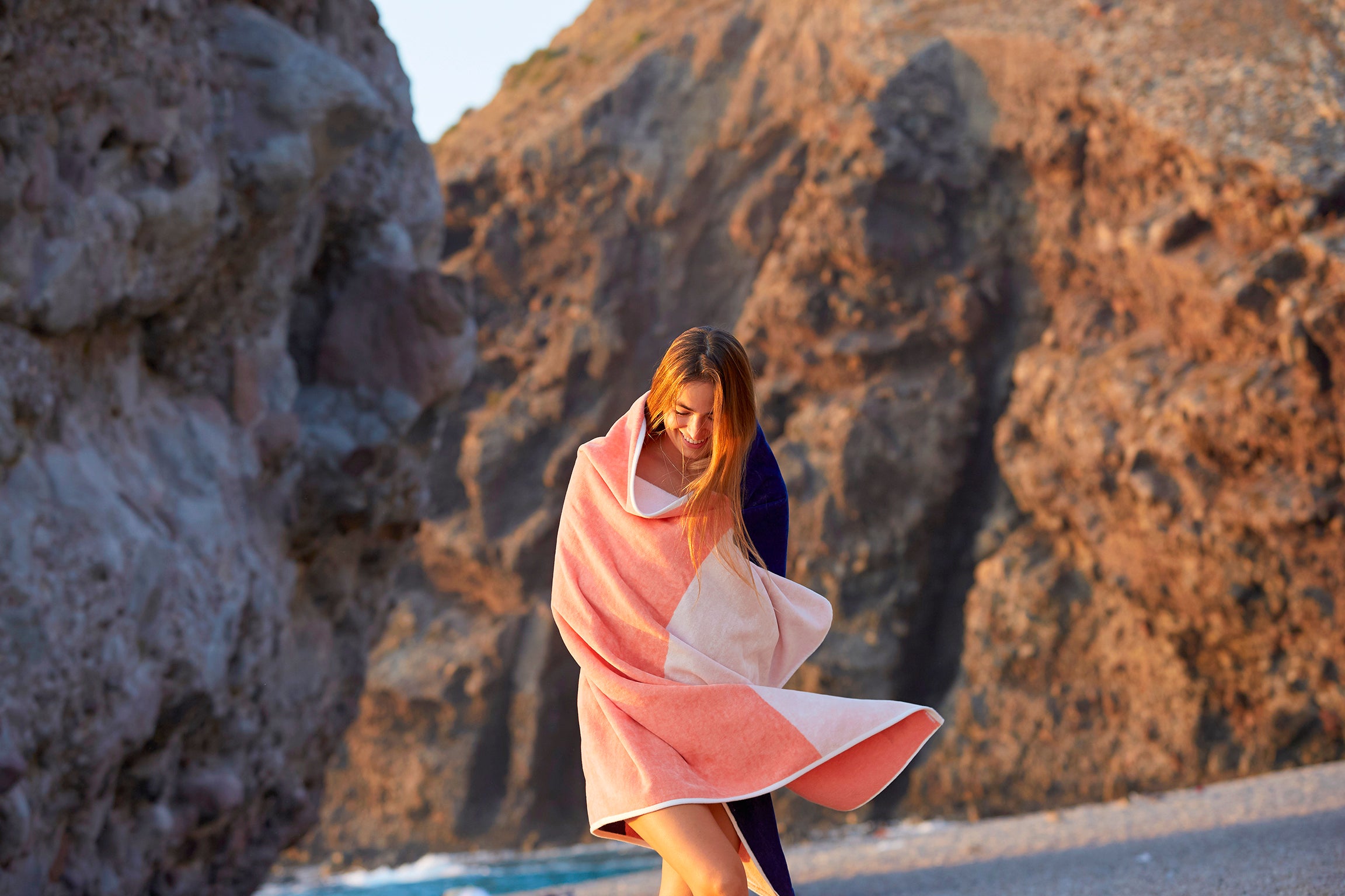 Girl embrazing a Tucca "Konoh" beach towel. Dark blue, creamy pink and white colors in big blocks composing a beautiful design. Large beach towel that doesn't get blown by the wind. Super soft texture as it i made with organic cotton.