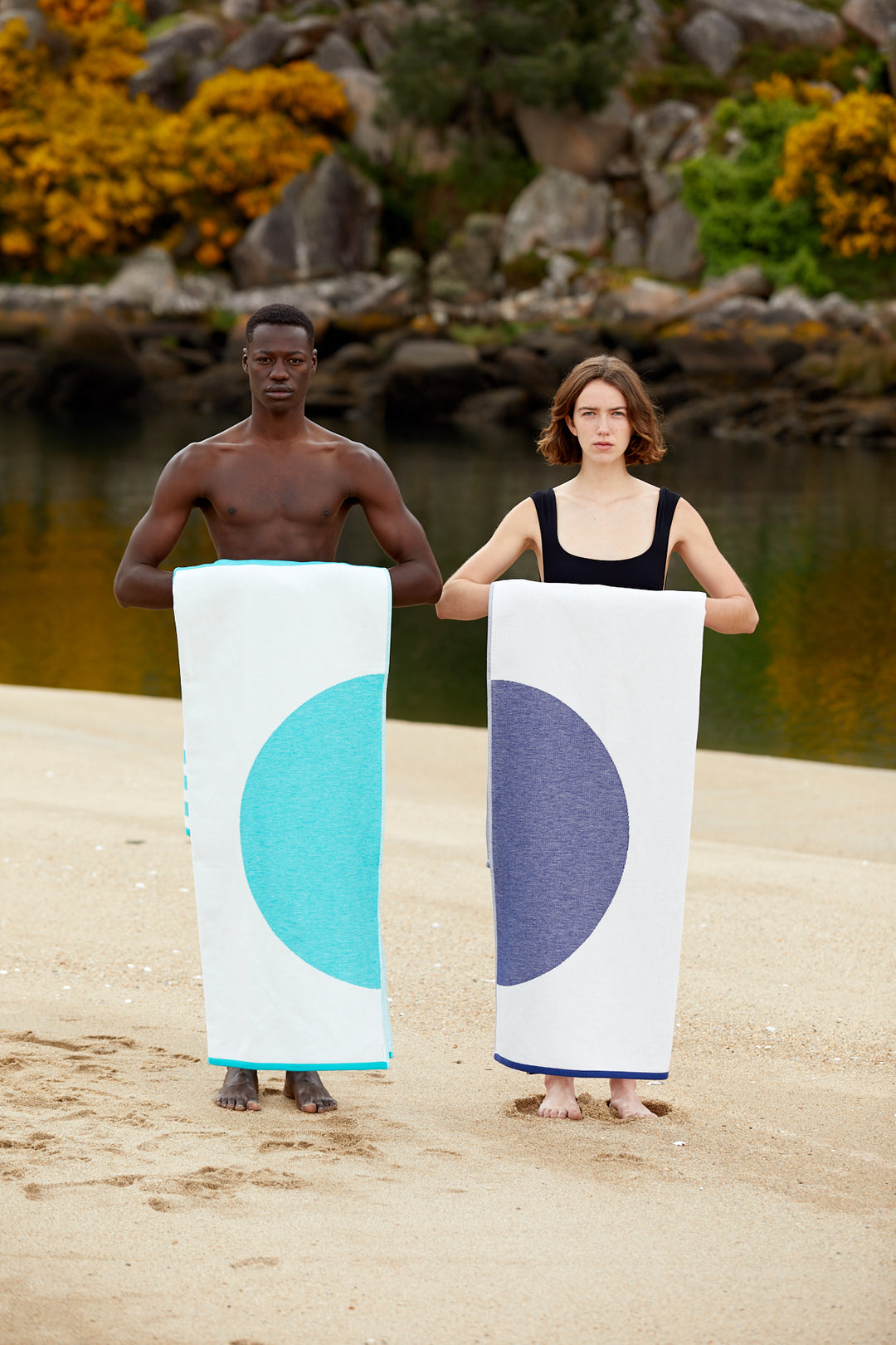 Girl and boy holding the Florid and Mayeri styles. Light and eco beach towels. Beautyful designs with blue and green colors. Super soft texture as it is made with 100% organic cotton in a sustainable way. Both stand up on the beach.