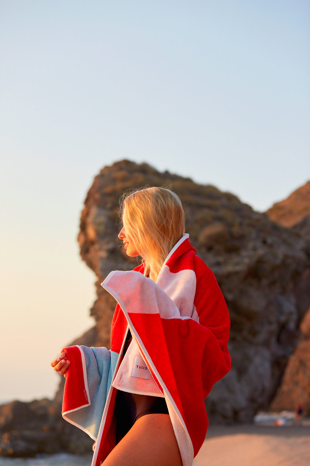 Girl embrazing a Tucca "Berry" beach towel. Light blue, red and white colors in big blocks composing a beautiful design.. Large beach towel that doesn't get blown by the wind. Super soft texture as it i made with organic cotton.