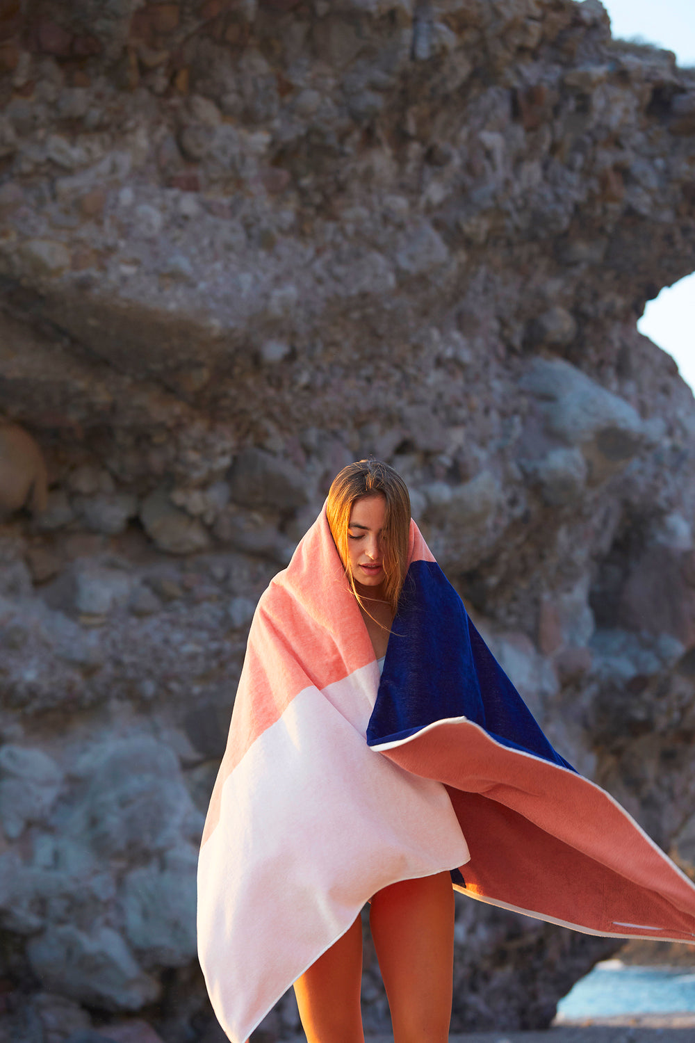 Girl embrazing a Tucca "Konoh" beach towel. Dark blue, creamy pink and white colors in big blocks composing a beautiful design. Large beach towel that doesn't get blown by the wind. Super soft texture as it i made with organic cotton.