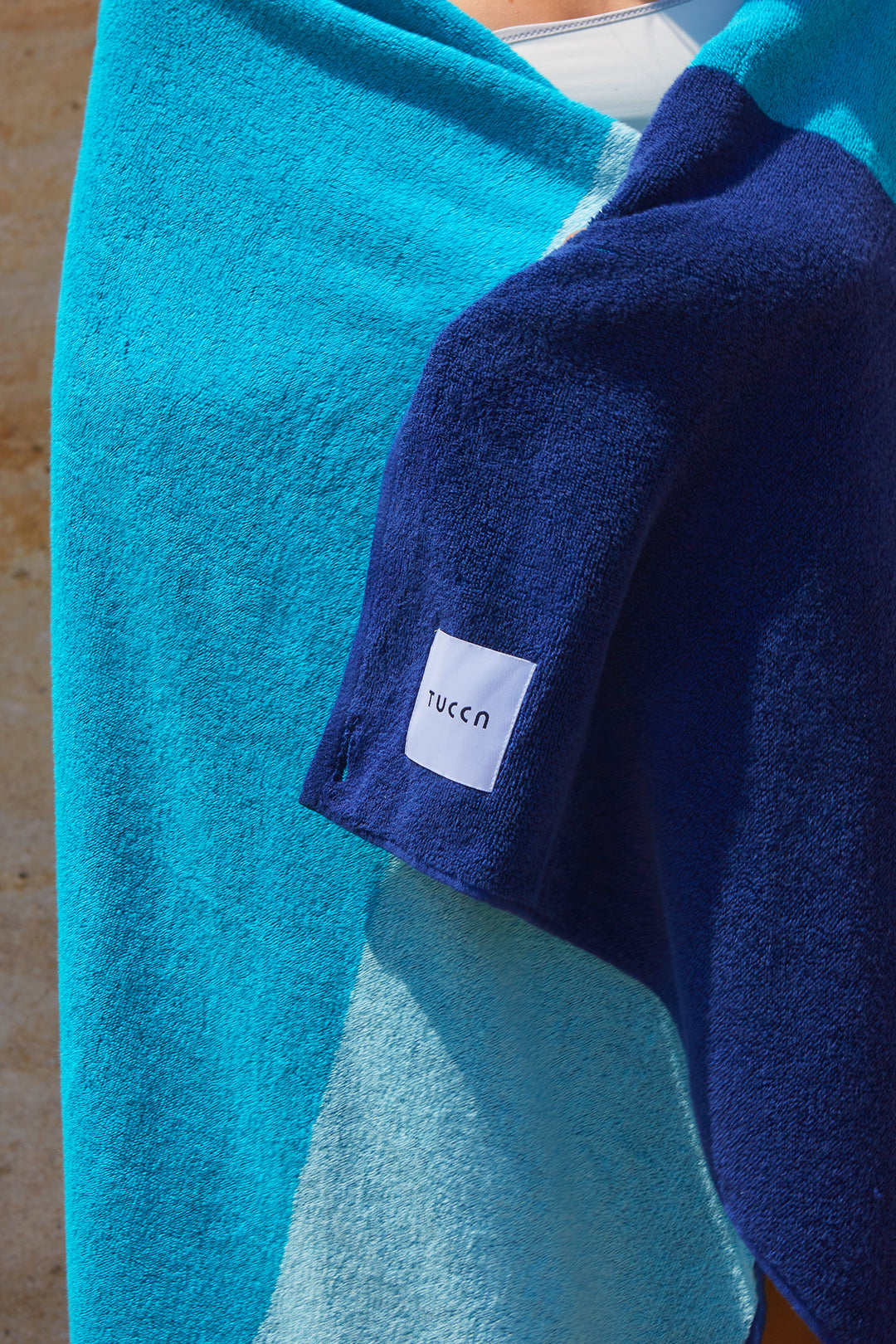 Girl embrazing a Tucca "Swell" beach towel. Light blue, green blue and dark blue colors in big blocks composing a beautiful design. Large beach towel that doesn't get blown by the wind. Thick and soft texture as it is made with 100% cotton.