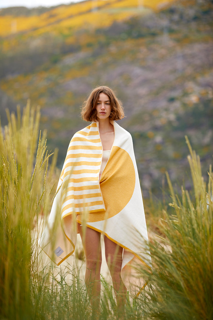 Girl covering herself with the Tucca "Danai" style. An extra light beach towel that doesn't get blown by the wind. Super soft texture as it is made with 100% organic cotton.